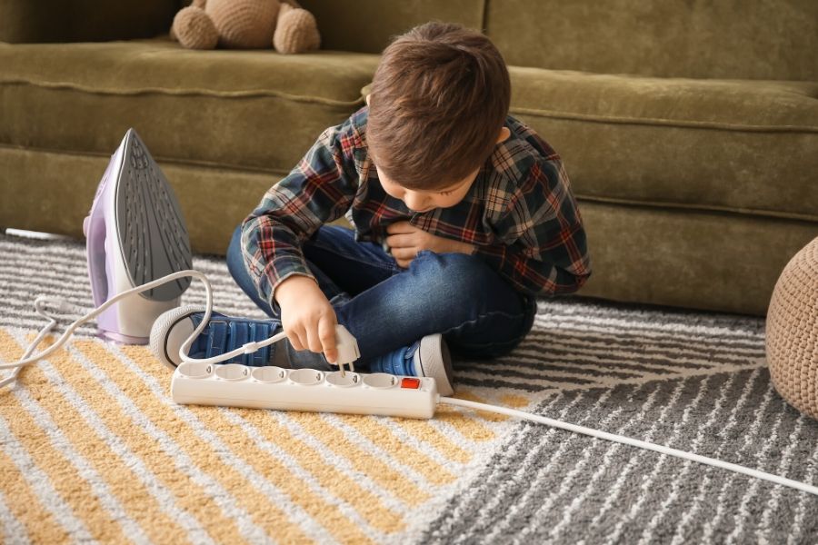 kid is playing with electric extension cord and iron at home